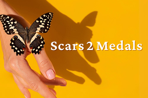 A butterfly lands on a woman's hand. The text reads Scars 2 Medals.