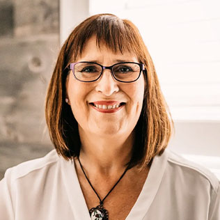 A woman with a brown hair in a long bob wearing glasses and a pendant necklace.